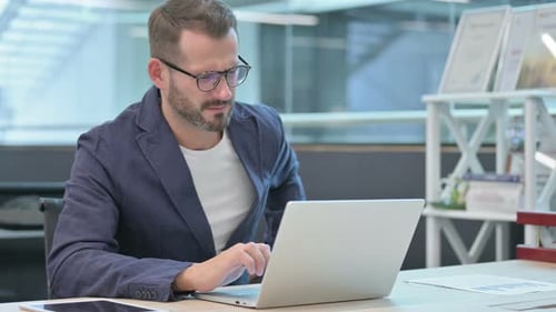 Middle Aged Businessman Having Back Pain While Using Laptop in Office
