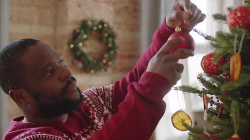 Man Decorating Christmas Tree with Red Ornaments