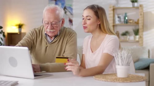 Woman Helps Senior Man Shop Online Using Laptop