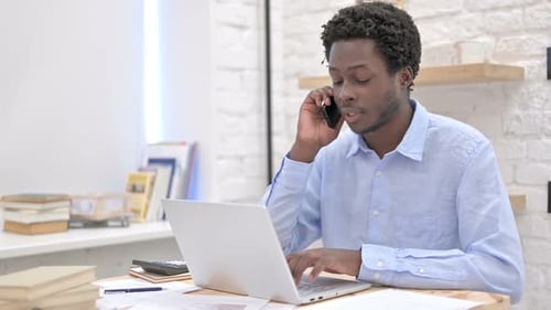 Man Works at Laptop, Talking on Mobile Phone
