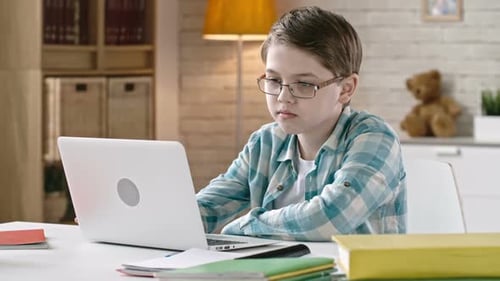 Boy with Glasses Typing on Laptop at Desk