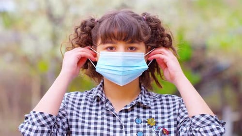 Girl Putting on Surgical Mask Outdoors