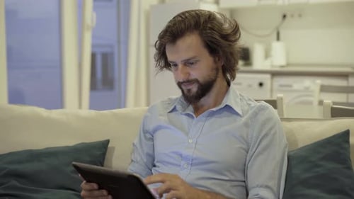 Man Using Tablet and Smiling on Couch