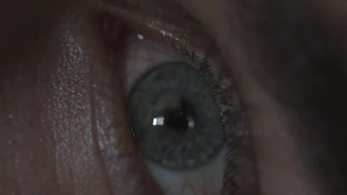 Macro close up of a man's eye opening, looking around, and looking at his phone.