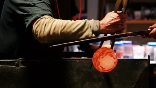 Glassblower Shaping Red-Spotted Glass Orb in Workshop