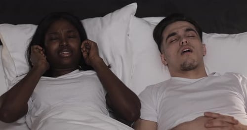 Couple multiethnique couché au lit ensemble. Une femme souffre du ronflement de son partenaire au lit