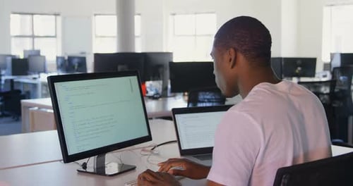 Rückansicht eines jungen schwarzen männlichen Managers, der am Desktop-PC und Laptop im modernen Büro arbeitet, 4k