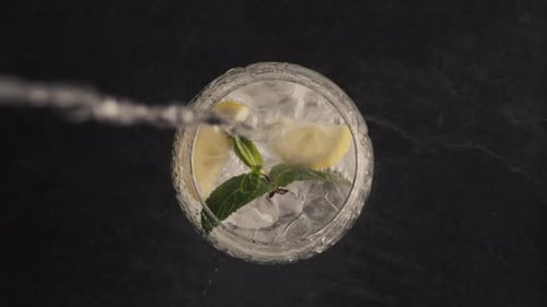 Pouring Beverage Into Clear Glass with Lemon and Mint