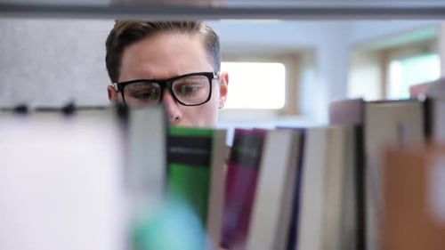College Library. Male Student Searching For Book On Bookshelves