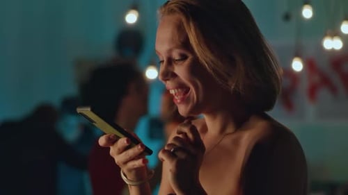 Woman Smiling at Phone at Lively Birthday Party