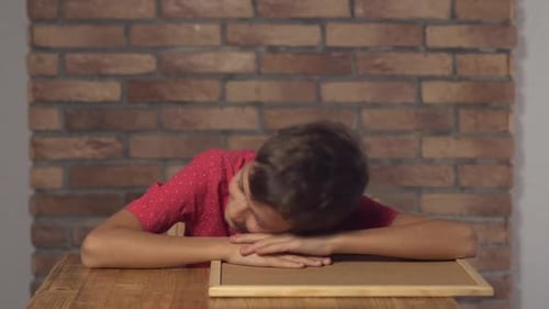 Kind sitzt am Schreibtisch mit Flipchart mit Schriftzug Wake Up auf dem Hintergrund Rote Backsteinmauer.