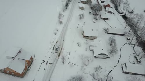 Fast Flight Over a Car Moving on Winter Road in Carpathian Village. Bird's Eye View of Snow-covered