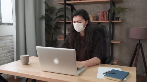 Young Business Woman Sneezes Into Protective Face Mask Working in the Office. Brunette Girl with