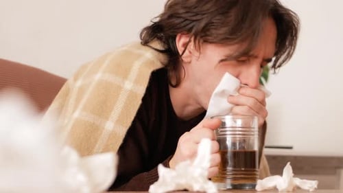 Sick Man Blowing Nose with Tissue at Home