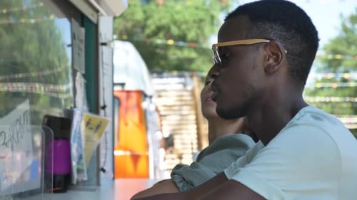 Black Man with His Caucasian Girlfriend are Sitting By a Street Food Van Waiting for an Order and