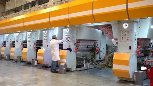 Adult Adjusts Settings on Printing Press in Factory