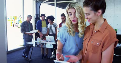 Women discussing over digital tablet with colleagues in background 4k