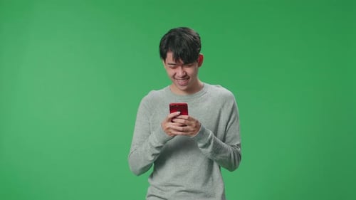 Ein asiatischer Mann benutzt gerne ein Handy, während er im Studio auf einem Greenscreen steht