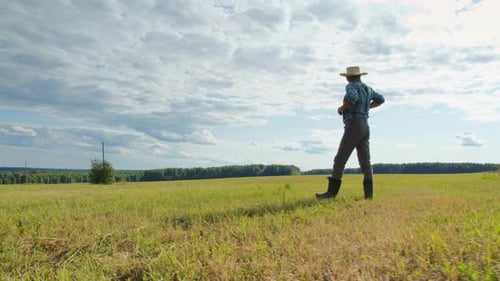 Farmer Wearing Straw Hat Suspenders and Rubber Boots Walking in Mown Field