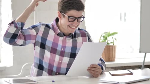 Excited Man Reading Document in Office Celebrates