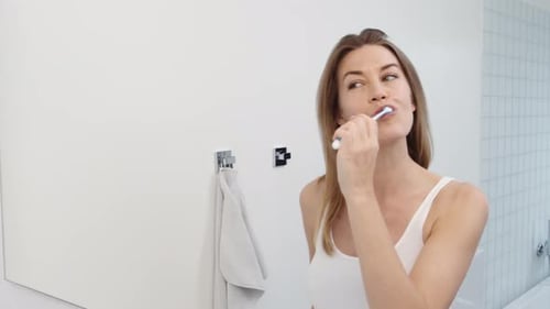 Woman Brushes Teeth in Bright Bathroom
