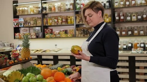 Woman Inspects Mangos at Market Fruit Display