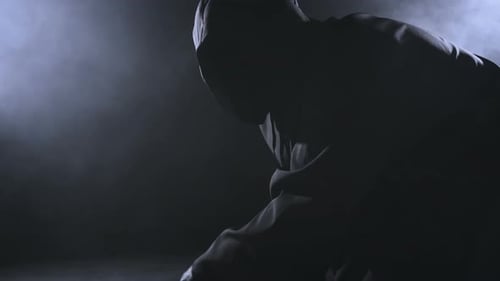 Hooded Figure Practicing with Sword in Dark Room