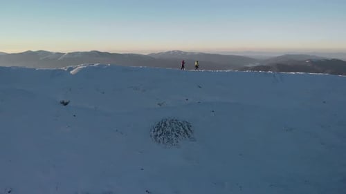 Drone Following Young Couple of Hikers, Walking on Mountain Ridge in Winter