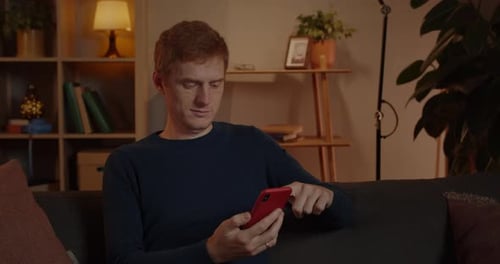 Crop View of Young Red Haired Man Scrolling Smartphone Screen While Sitting on Couch at Home in