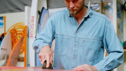 Man Repairing a Surfboard in a Workshop