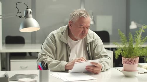 An Elderly Man at an Office Desk Coughs Holds His Hand to His Chest and Head Takes a Napkin