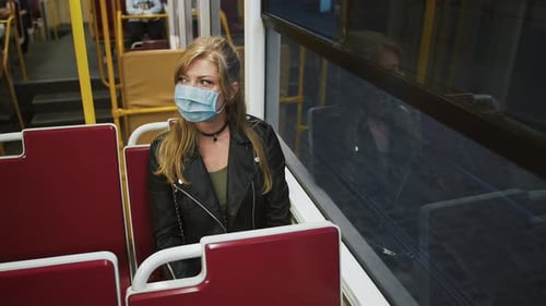 Young Lady Hipster in Protective Mask is Riding a Tram Sitting on Seat and Looking Out the Window