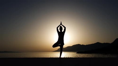 Silhouette de femme pratiquant le yoga au coucher du soleil par la mer