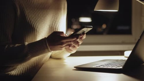 Woman Using Cellphone Next to Laptop at Night