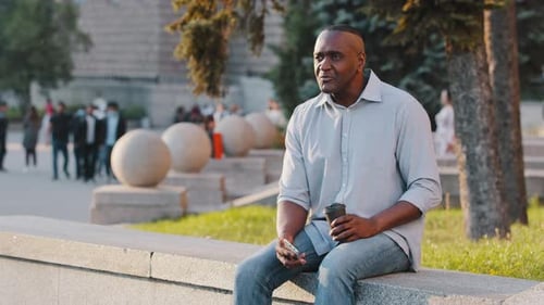 Man Sits and Drinks Coffee in Urban Park