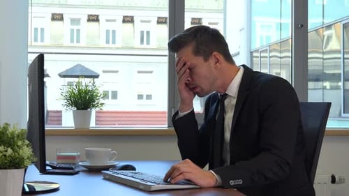 An office worker in a suit in front of a computer gets upset