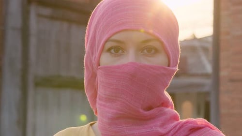 Attraktive muslimische Frau mit natürlichem Make-up im rosa Hijab-Schal schaut in die Kamera