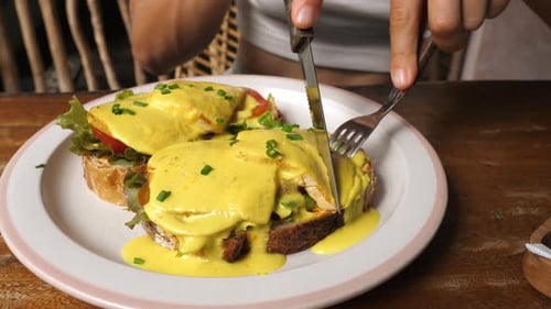 Cutting Delicious Eggs Benedict with Knife and Fork