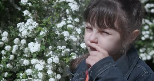 Young Girl Reacts to Allergies near Flowering Bush