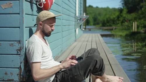 Modern American Businessman is Using Laptop for Remote Work Sitting on Wooden Pier By Lake Spbd