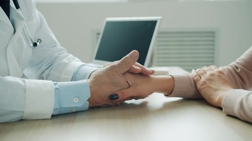 Male Doctor Holding Female Patient's Hand Supporting Woman in Hospital Office