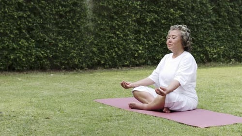 Senior Woman Meditating Peacefully Outdoors on Lawn