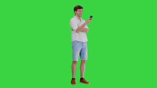 Handsome Young Man Using His Smartphone and Laughing on a Green Screen, Chroma Key.