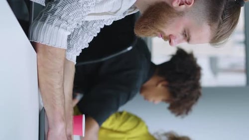 Bärtiger Mann mit vertikalem Bildschirm, der im Büro arbeitet und Laptop benutzt