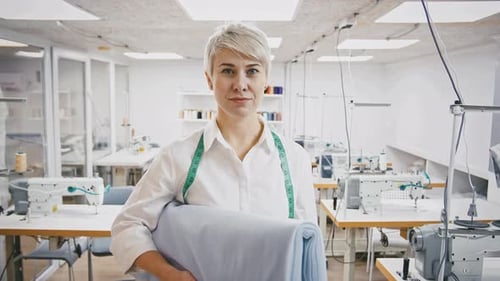 Young Woman Tailor or Fashion Designer Holding Piece of Fabric and Smiling Posing at Sewing Workshop