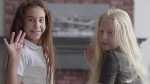 Two Smiling Girls Waving to Camera Indoors