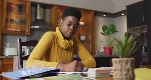 Woman Writes in Notebook at Kitchen Table
