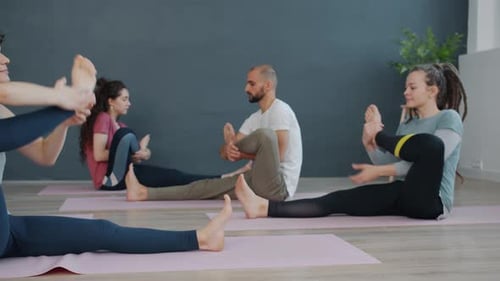 Attractive Women and Man Doing Yoga in Class Stretching Legs Sitting on Mats