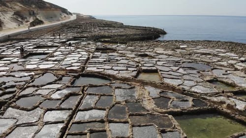An aerial drone shot flying in reverse across the ancient rocky Salt Pans of Gozo Island in Malta.