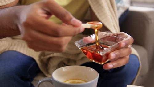 Sick Young Man Adding Honey To Hot Tea at Home